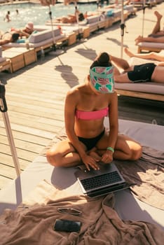 beautiful girl in bikini is typing on a laptop and sunbathing on the beach. High quality photo