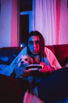 Close up portrait of A gamer or a streamer girl at home in a dark room with a game controller playing with her dog and sits in front of a monitor or TV. High quality photo
