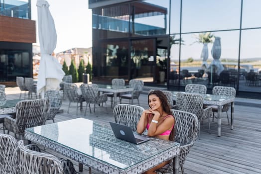 Cute young woman sitting on terrace, while using laptop for work at summer day