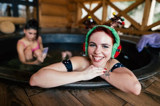 Young girls in bikinis bathing in an outdoor bathtub on winter holidays. Wooden cottage. High quality photo