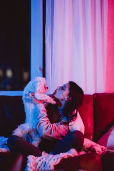 Beautiful young girl watching movie at home in a dark room with a popcorn bucket and playing with her dog and sits in front of a monitor or TV watching movie. Crazy emotions. High quality photo