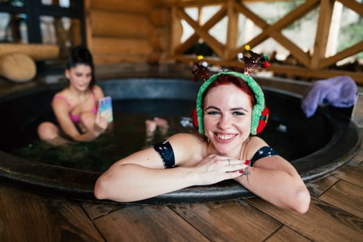 Young girls in bikinis bathing in an outdoor bathtub on winter holidays. Wooden cottage. High quality photo