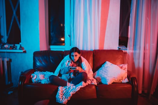A gamer or a streamer girl at home in a dark room with a game controller playing with her dog and sits in front of a monitor or TV. High quality photo