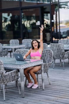 Cute young woman sitting on terrace, happy with hands up winner at summer day