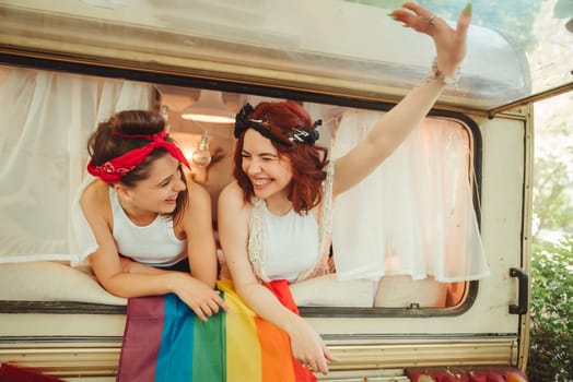 Portrait of a cute lesbian couple. Two girls spend time tenderly together watching movie on laptop in a camper trailer with LGBT flag on the wall. Love and attitude. LGBT concept. High quality photo