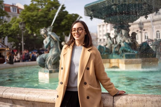 Female tourist enjoying in Lisbon downtown, Portugal. Sunny day. Travel Europe concept. woman dressed stylish coat sitting in front of baroque fountains on Rossio Square, Lisbon. Looking at camera