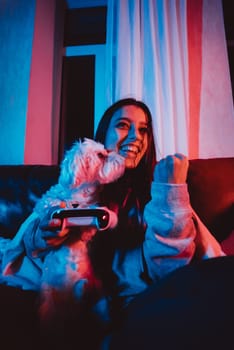 A gamer or a streamer girl at home in a dark room with a game controller playing with her dog and sits in front of a monitor or TV. High quality photo