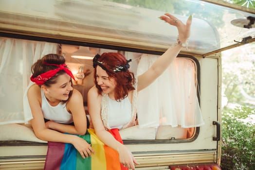 Portrait of a cute lesbian couple. Two girls spend time tenderly together watching movie on laptop in a camper trailer with LGBT flag on the wall. Love and attitude. LGBT concept. High quality photo