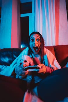 Close up portrait of A gamer or a streamer girl at home in a dark room with a game controller playing with her dog and sits in front of a monitor or TV. High quality photo