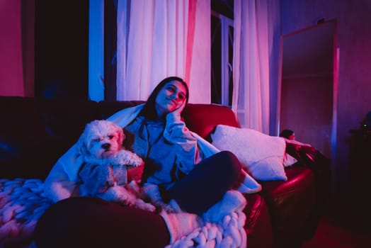Beautiful young girl at home in a dark room playing with her dog and sits in front of a monitor or TV. High quality photo