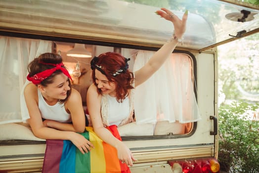 Portrait of a cute lesbian couple. Two girls spend time tenderly together watching movie on laptop in a camper trailer with LGBT flag on the wall. Love and attitude. LGBT concept. High quality photo