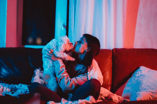 Beautiful young girl watching movie at home in a dark room with a popcorn bucket and playing with her dog and sits in front of a monitor or TV watching movie. Crazy emotions. High quality photo