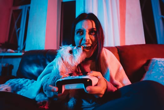 Close up portrait of A gamer or a streamer girl at home in a dark room with a game controller playing with her dog and sits in front of a monitor or TV. Crazy emotions. High quality photo