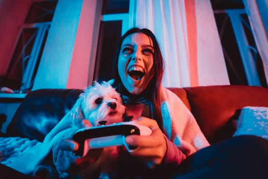 Close up portrait of A gamer or a streamer girl at home in a dark room with a game controller playing with her dog and sits in front of a monitor or TV. Crazy emotions. High quality photo