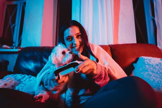 Close up portrait of A gamer or a streamer girl at home in a dark room with a game controller playing with her dog and sits in front of a monitor or TV. Crazy emotions. High quality photo