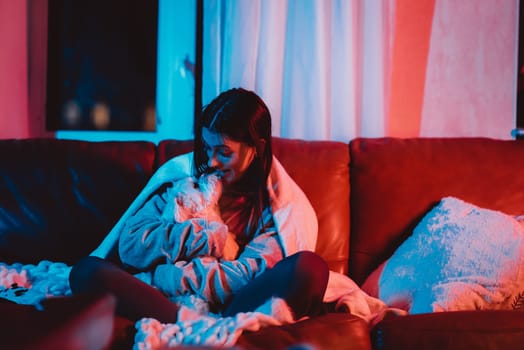 Beautiful young girl watching movie at home in a dark room with a popcorn bucket and playing with her dog and sits in front of a monitor or TV watching movie. Crazy emotions. High quality photo