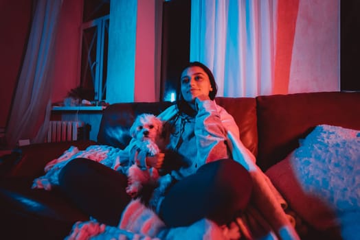 Close up portrait of A gamer or a streamer girl at home in a dark room with a game controller playing with her dog and sits in front of a monitor or TV. High quality photo