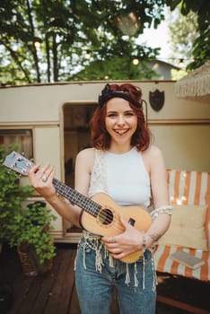 Happy hippie girl is having a good time with playing on guitar in camper trailer. Holiday, vacation, trip concept.High quality photo