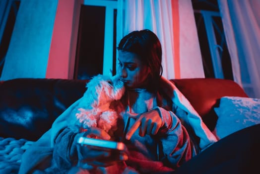 Beautiful young girl at home in a dark room playing with her dog and sits in front of a monitor or TV. High quality photo