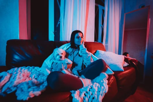 Beautiful young girl at home in a dark room playing with her dog and sits in front of a monitor or TV. High quality photo