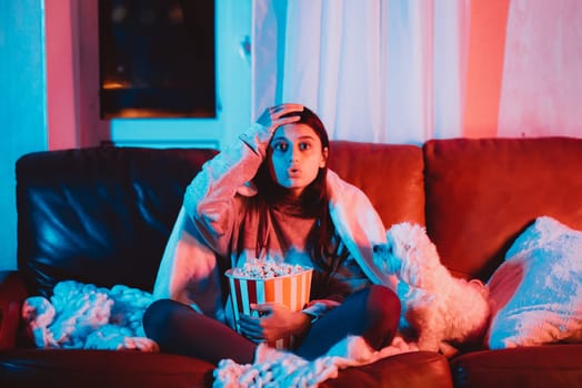 A gamer or a streamer girl at home in a dark room with a popcorn bucket playing with her dog and sits in front of a monitor or TV. High quality photo