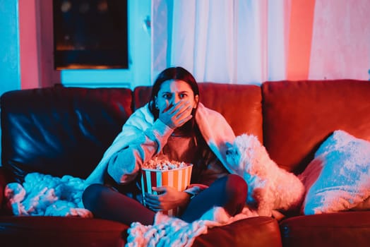 Beautiful young girl at home in a dark room with a popcorn bucket playing with her dog and sits in front of a monitor or TV watching movie. High quality photo