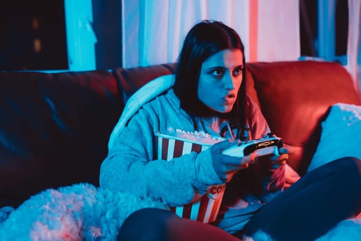 A gamer or a streamer girl at home in a dark room with a game controller and popcorn bucket playing with her dog and sits in front of a monitor or TV. High quality photo