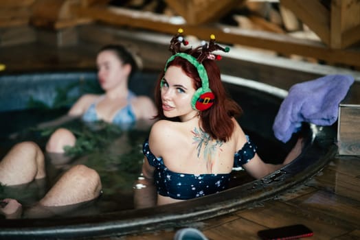 Young girls in bikinis bathing in an outdoor bathtub on winter holidays. Wooden cottage. High quality photo