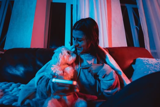 Beautiful young girl at home in a dark room playing with her dog and sits in front of a monitor or TV. High quality photo