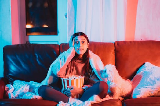 A gamer or a streamer girl at home in a dark room with a popcorn bucket playing with her dog and sits in front of a monitor or TV. High quality photo