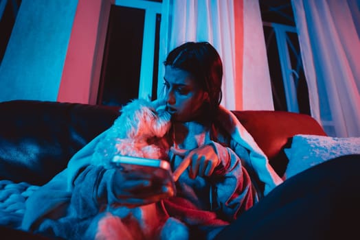 Beautiful young girl at home in a dark room playing with her dog and sits in front of a monitor or TV. High quality photo