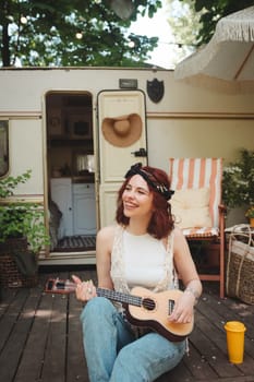 Happy hippie girl are having a good time with playing on guitar in camper trailer. Holiday, vacation, trip concept.High quality photo