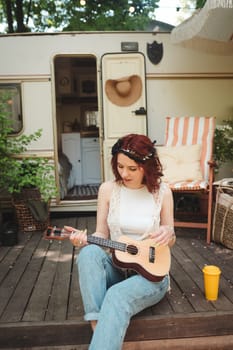 Happy hippie girl are having a good time with playing on guitar in camper trailer. Holiday, vacation, trip concept.High quality photo