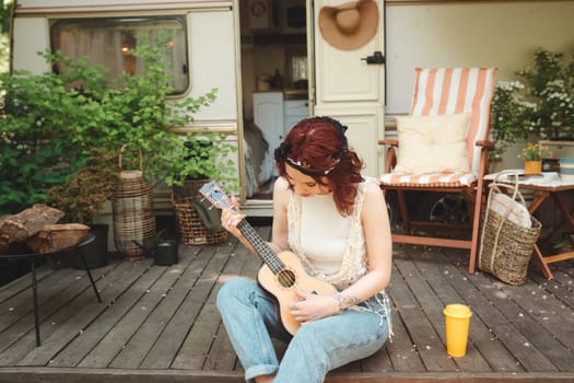Happy hippie girl are having a good time with playing on guitar in camper trailer. Holiday, vacation, trip concept.High quality photo
