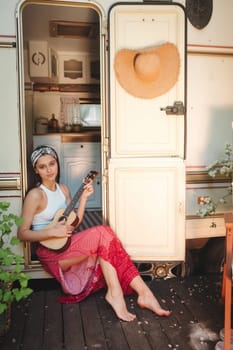 Happy hippie girl are having a good time with playing on guitar in camper trailer. Holiday, vacation, trip concept.High quality photo