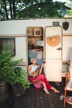 Happy hippie girl are having a good time with playing on guitar in camper trailer. Holiday, vacation, trip concept.High quality photo