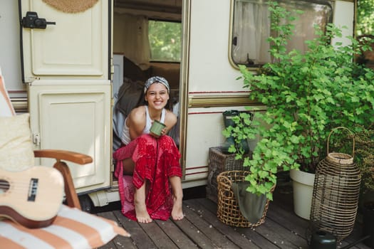 Happy hippie girl are having a good time with cup of tea in camper trailer. Holiday, vacation, trip concept.High quality photo