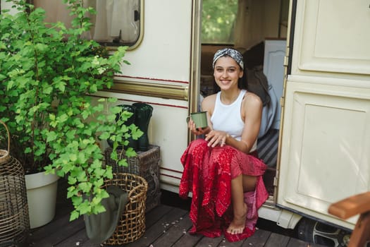 Happy hippie girl are having a good time with cup of tea in camper trailer. Holiday, vacation, trip concept.High quality photo