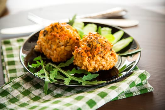Cooked meatballs in a plate with fresh vegetables, on a wooden table.