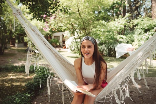 Happy hippie girl is reading a book in hammock having a good time with playing in camper trailer. Holiday, vacation, trip concept.High quality photo