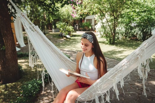 Happy hippie girl is reading a book in hammock having a good time with playing in camper trailer. Holiday, vacation, trip concept.High quality photo