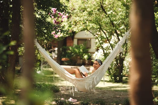 Happy hippie girl is reading a book in hammock having a good time with playing in camper trailer. Holiday, vacation, trip concept.High quality photo