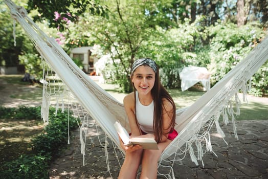 Happy hippie girl is reading a book in hammock having a good time with playing in camper trailer. Holiday, vacation, trip concept.High quality photo