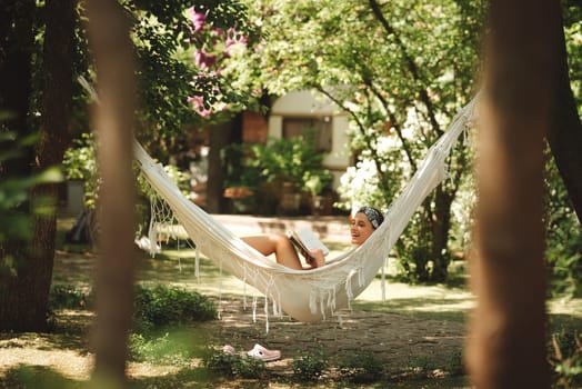 Happy hippie girl is reading a book in hammock having a good time with playing in camper trailer. Holiday, vacation, trip concept.High quality photo