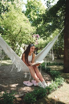 Happy hippie girl is reading a book in hammock having a good time with playing in camper trailer. Holiday, vacation, trip concept.High quality photo