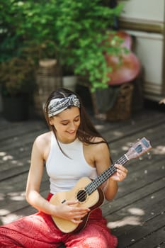 Happy hippie girl are having a good time with playing on guitar in camper trailer. Holiday, vacation, trip concept.High quality photo