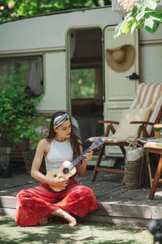 Happy hippie girl are having a good time with playing on guitar in camper trailer. Holiday, vacation, trip concept.High quality photo