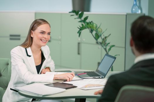 Smiling professional HR agent making a job interview to a applicant in the bright modern office. Young woman interviewing young freelancer for job position.