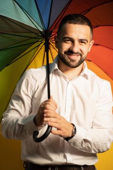 Young straight man with a rainbow umbrella behind his back. Healthy fashion lifestyle, people sincere emotions, cold season concept. Handsome guy in support of LGBTQ society.