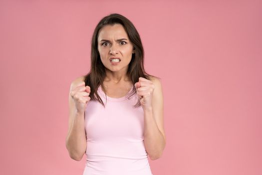 Showing ager beautiful young woman wearing pink t-shirt holding hands gathered in fists, Female half-length portrait. Human emotions, facial expression concept.